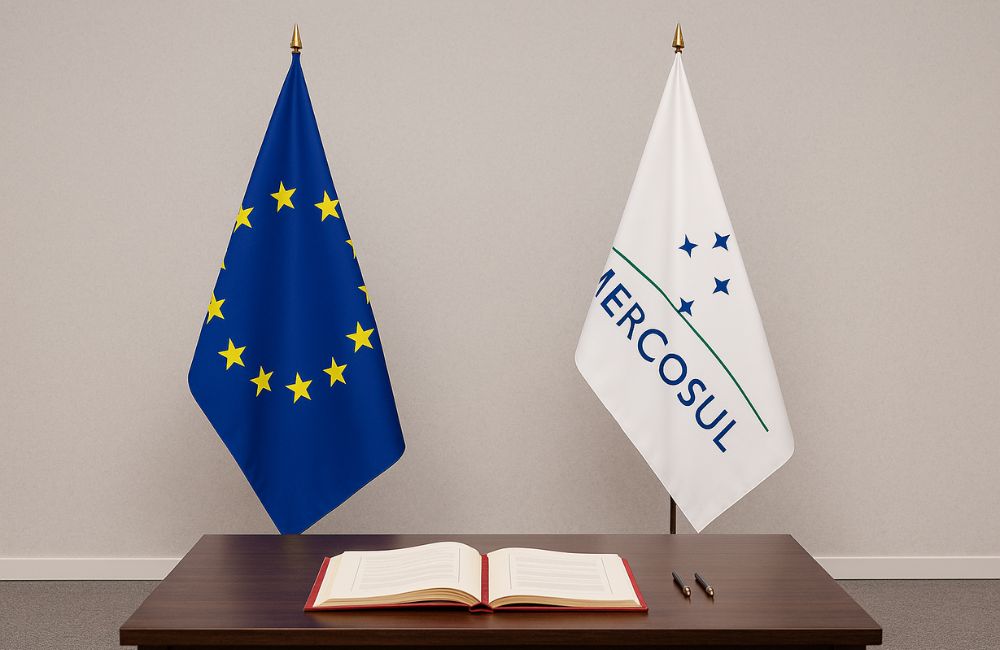 Bandeiras da UE e do Mercosul com mesa de assinatura ao fundo, destacando o Acordo União Europeia‑Mercosul
